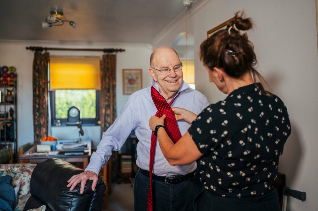 Woman helping man to dress by doing up his tie up and get ready for the day at home