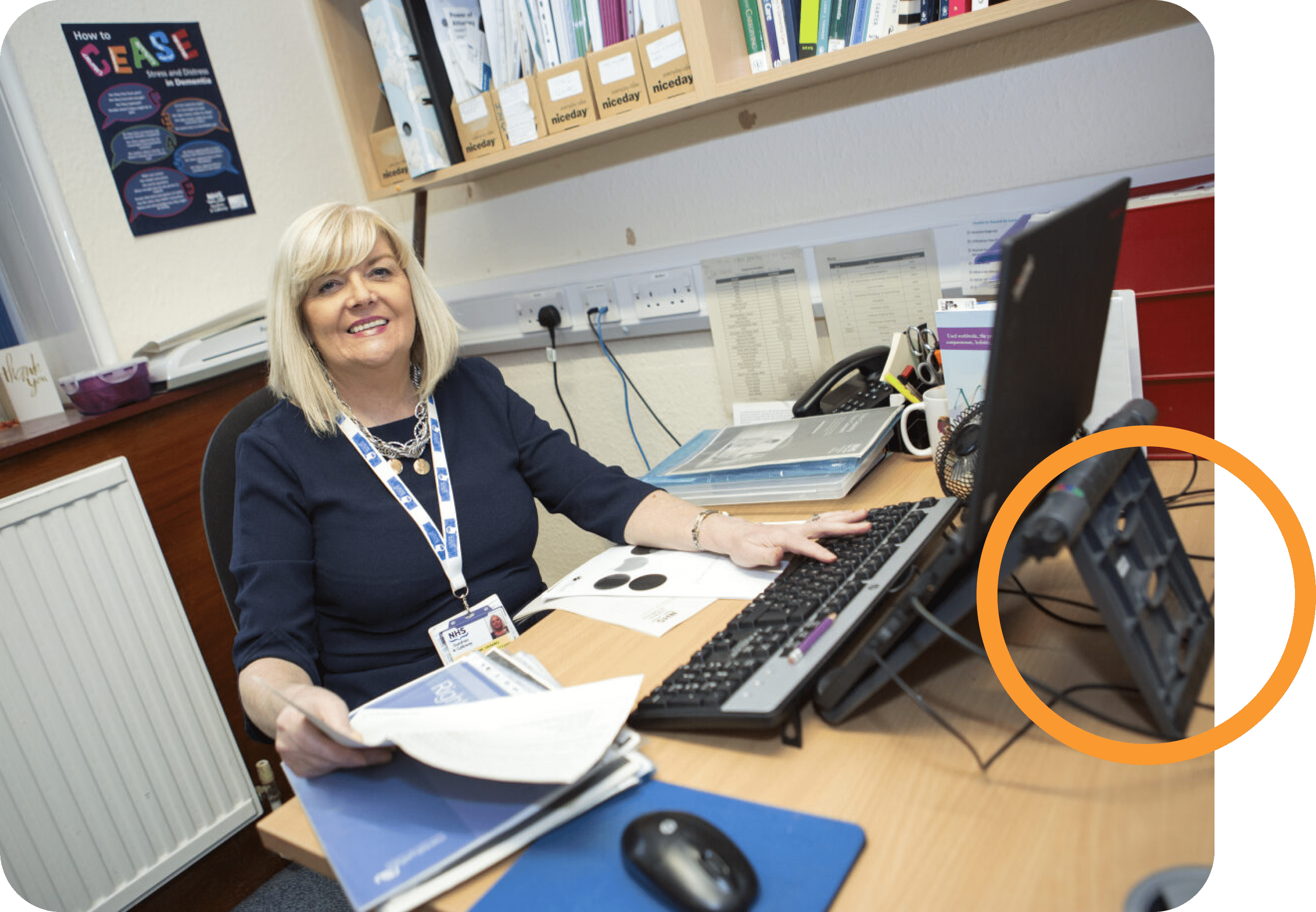 A lady sat at her desk smiling with some paperwork in hand