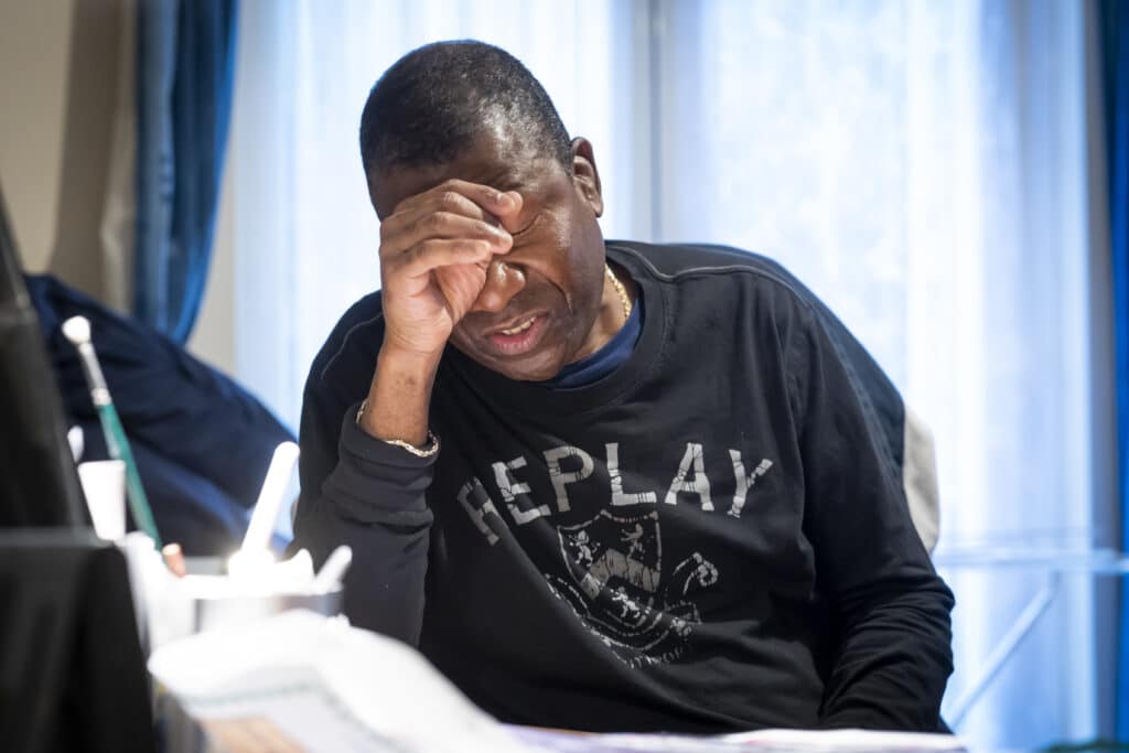 Man sitting down slumped with hand covering his face looking tired and surrounded by paperwork