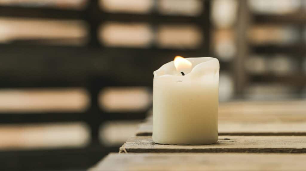 A single white candle burns on a table in a room with low light