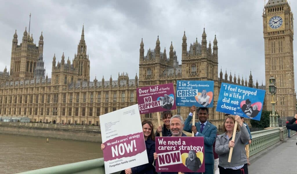 A small group of smiling protesters holding placards stand on Westminster Bridge with the houses of parliament in the background