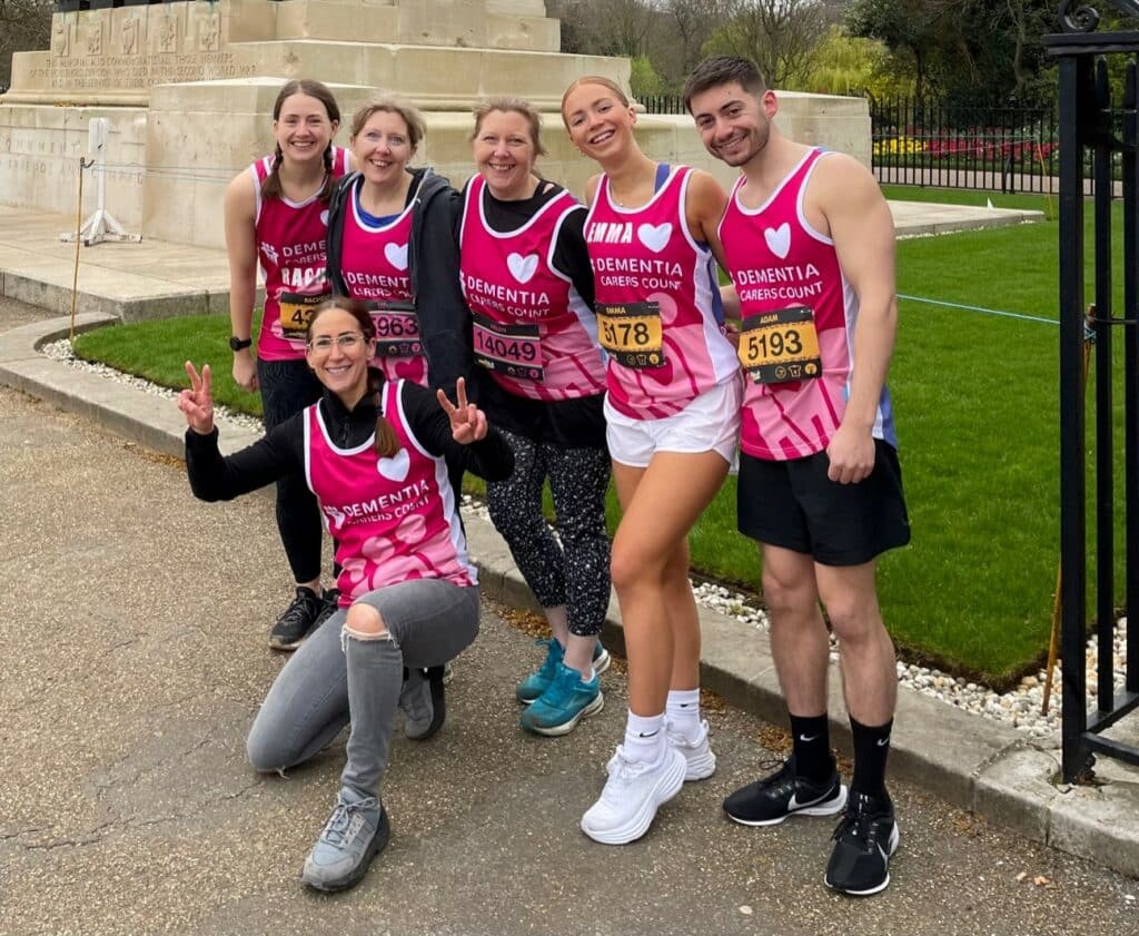 Group of happy athletes wearing Dementia Carers Count purple running vests stand in a group smiling for the camera