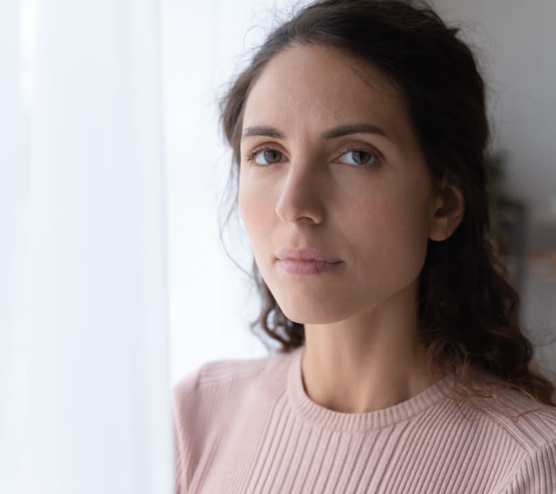 A portrait photo of a woman standing alone next to a window looking calm and determined