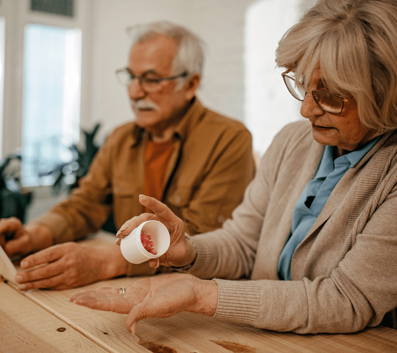 A dementia carer handles medication. Her husband is in the background.