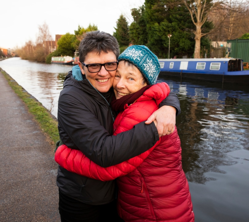 Two women smile as they embrace by a canal