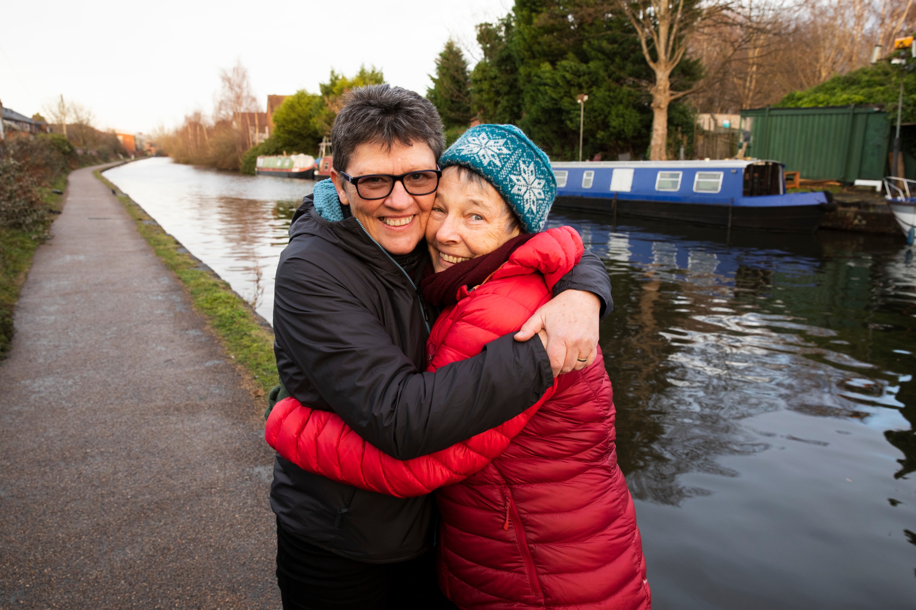 Two women smile as they embrace by a canal
