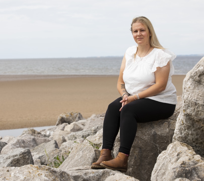 A woman is sitting on a rock on a beach looking at the camera