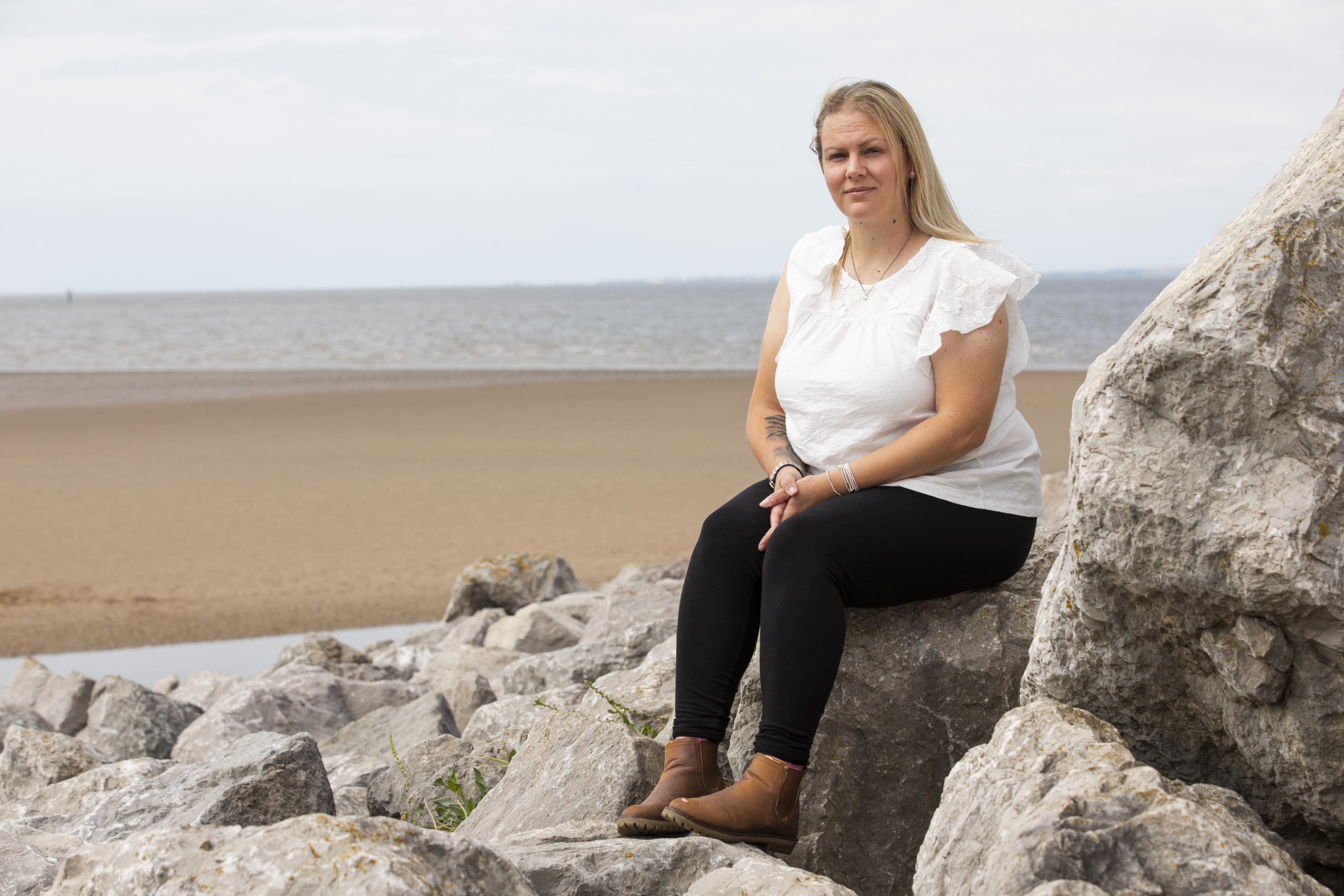 A woman is sitting on a rock on a beach looking at the camera
