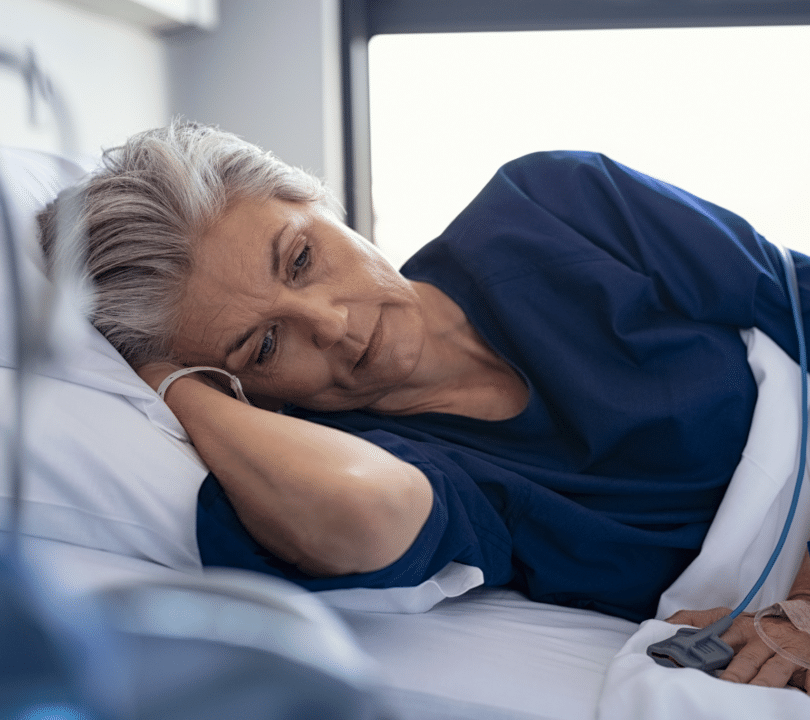 A woman is lying in bed looking very unwell. She has been admitted to hospital in an emergency.