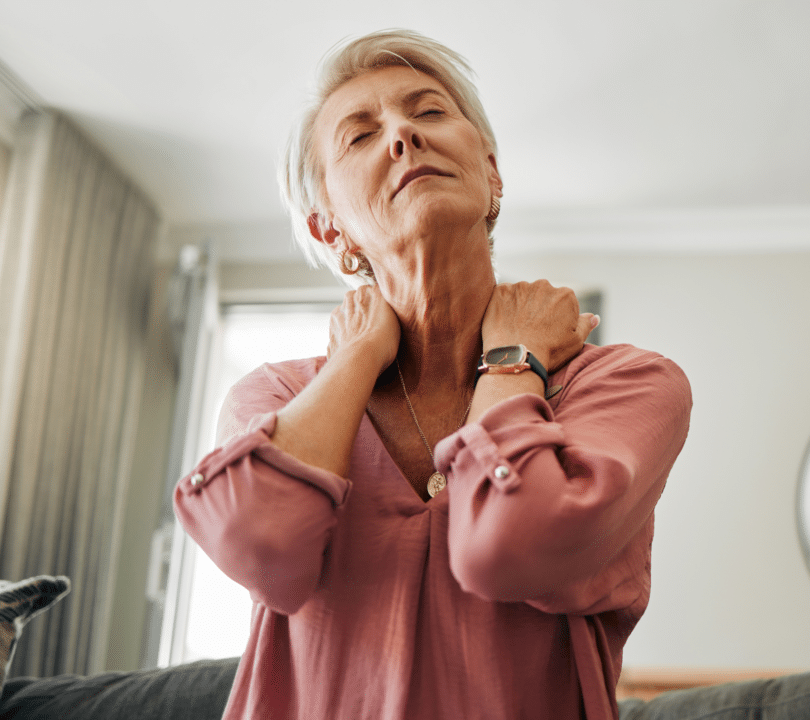 A woman is rubbing her shoulders and looks tired and in discomfort. She has no time to look after her health needs.