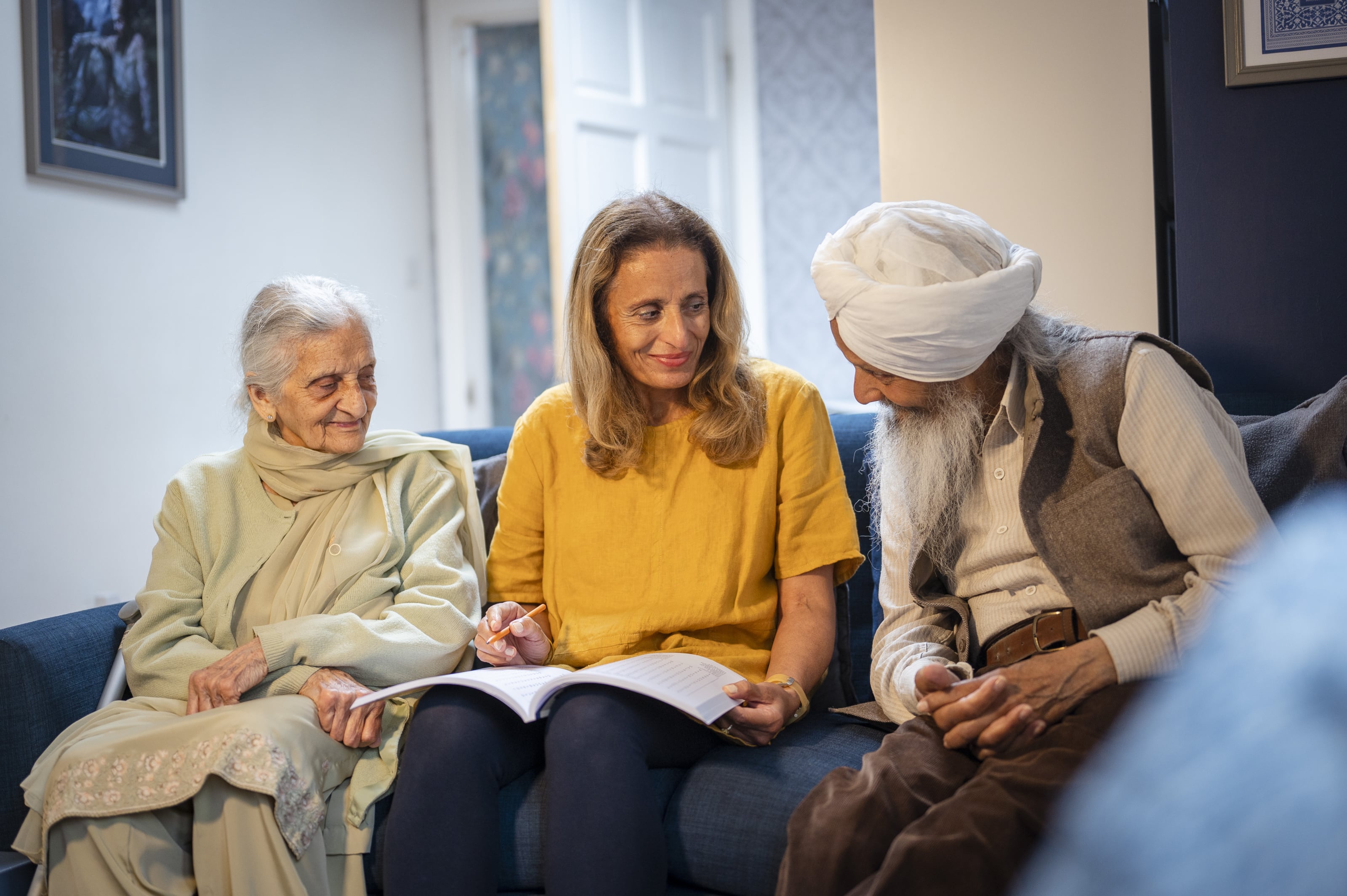 A woman is sat between a couple in their own home going through some papers with them. She is smiling, listening to them and looks calm.